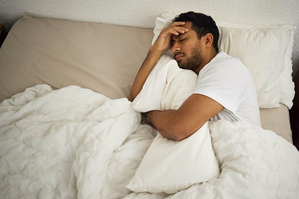 How I long to have you by my side. a man cuddling a pillow while sleeping in his bed.