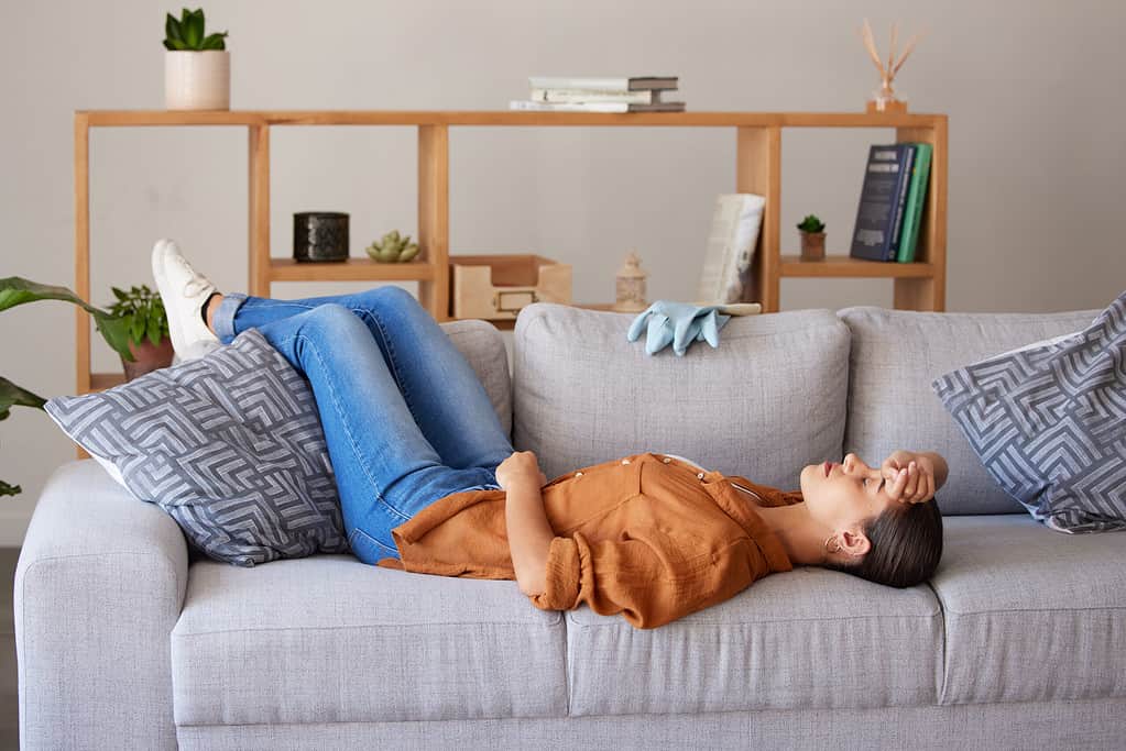 Tired cleaner woman, sleep and sofa to relax for fatigue, wellness and mental health after cleaning house. Hygiene expert, burnout and sleeping on living room couch for rest, health or stress in home